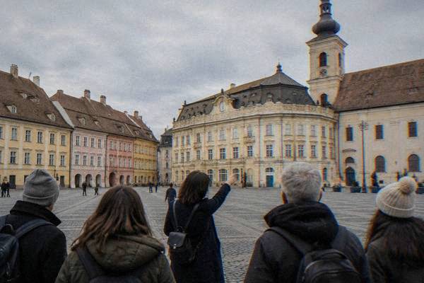 A small group follows a guide across the cobbles of an old town square in Sibiu.