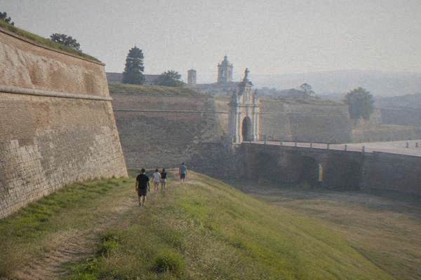 A small group walking along the sloping grass bank below the massive stone and brick walls of a star-shaped fortress, Alba Iulia