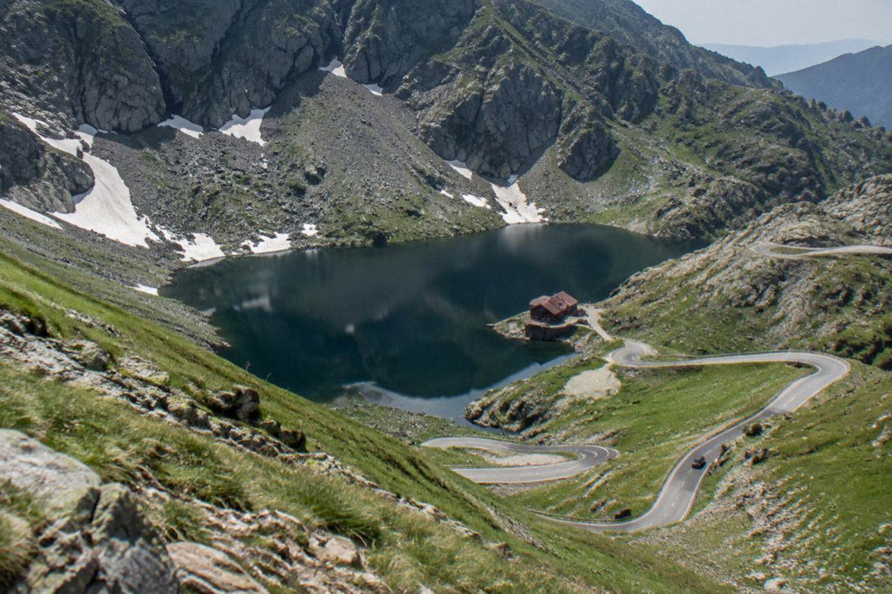 A glacial lake ringed by steep mountain slopes with a road switchbacking down toward the shore