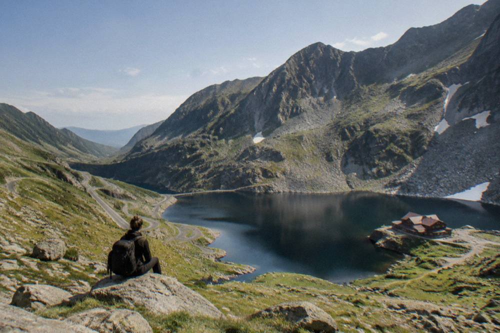 A mountain road with hairpin bends descending toward a calm lake between ridges