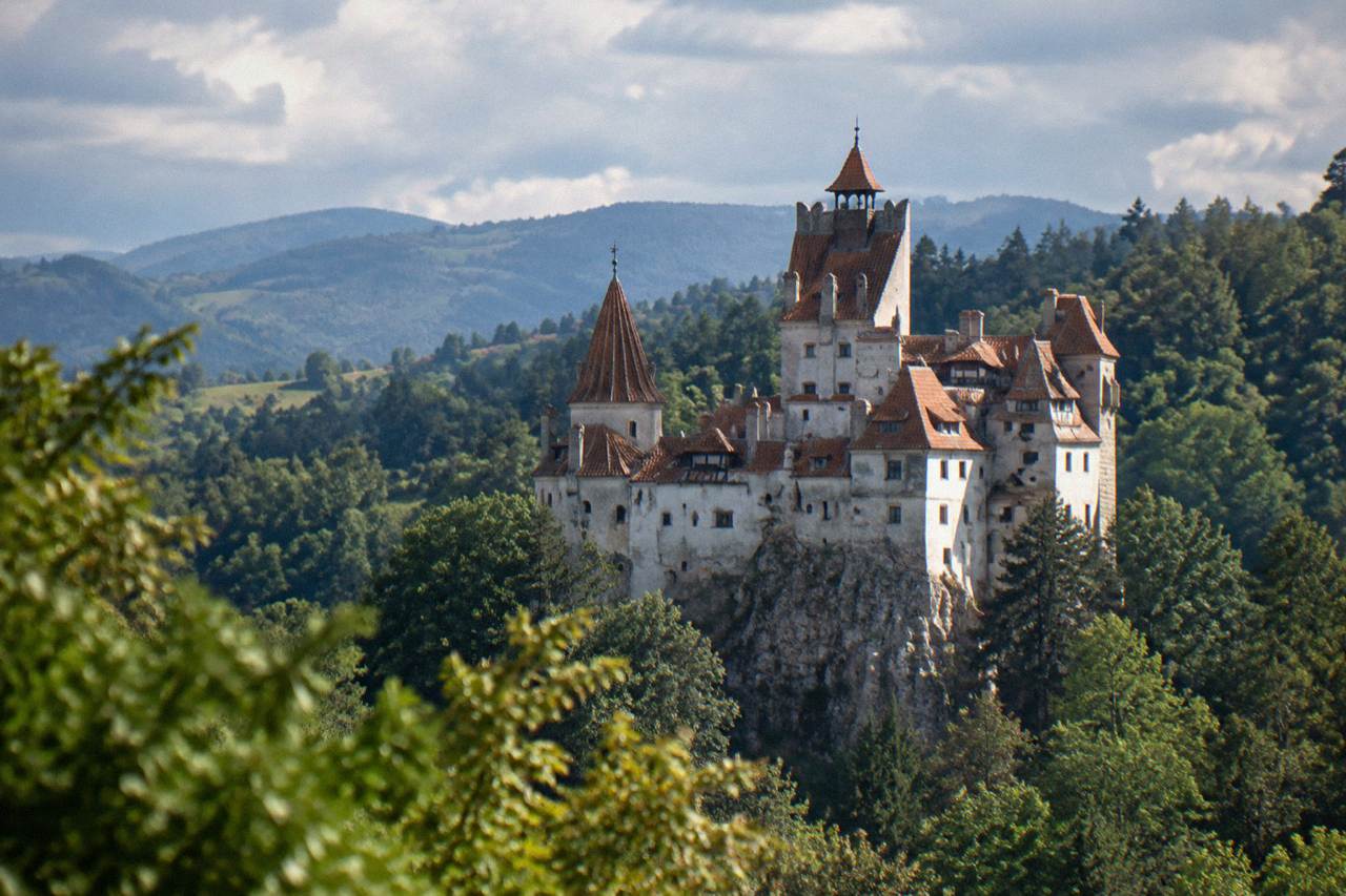 The white walls and red-tiled roofs of Bran Castle rising above forested hills in Transylvania