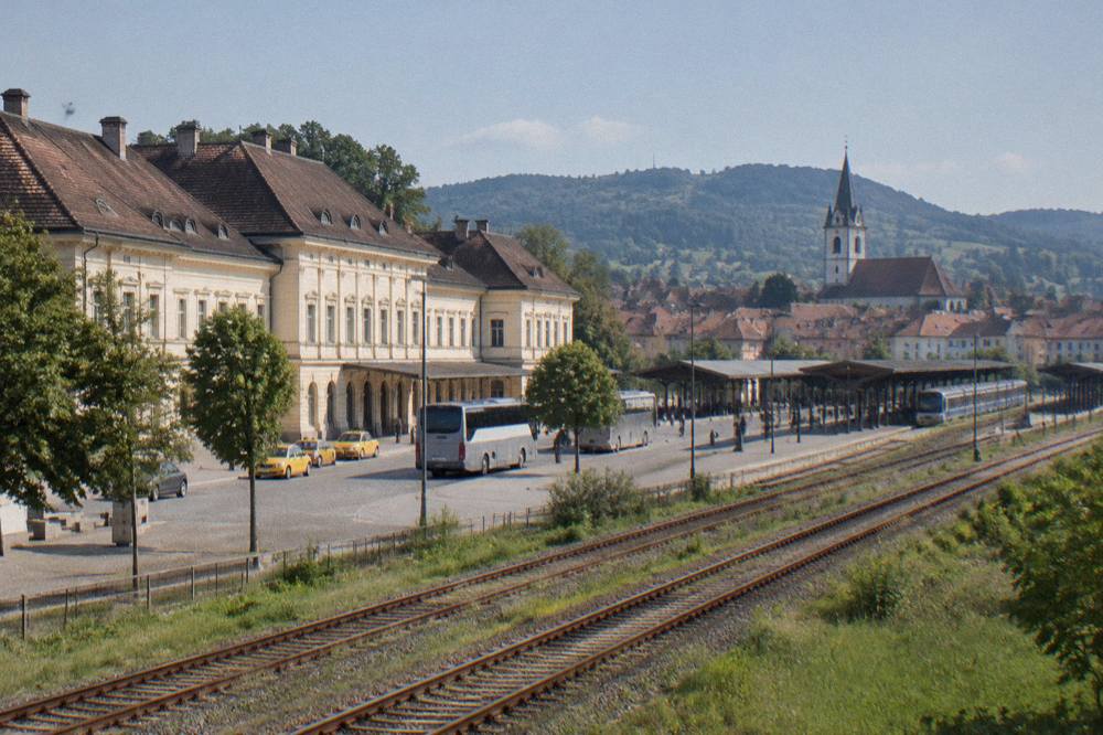 Railway tracks curving through green Transylvanian countryside with a village church tower in the distance
