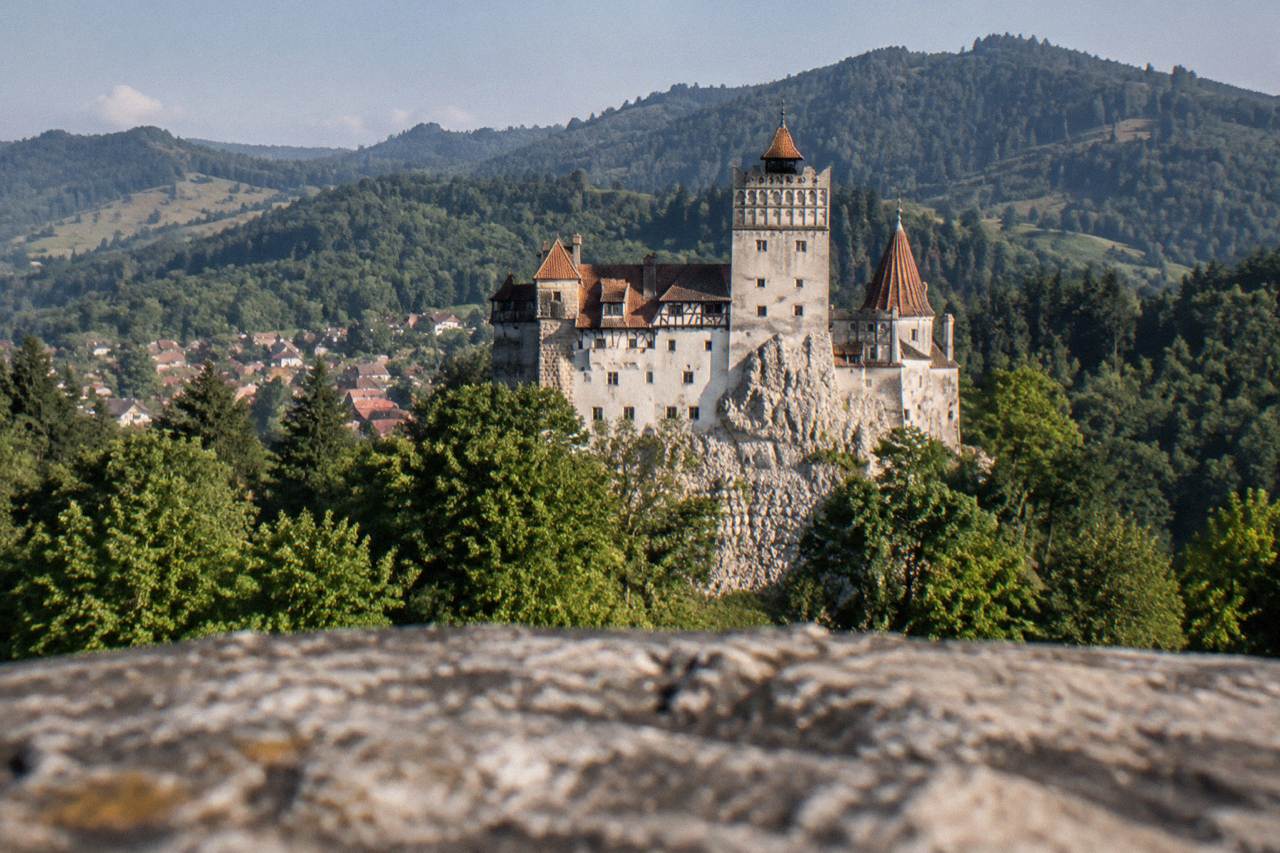 Bran Castle standing on a rocky hill above a village in Transylvania, with forested Carpathian slopes behind it