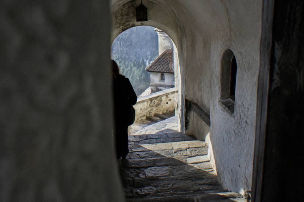 A stone passageway inside Bran Castle with arched doorways, worn steps and shafts of daylight