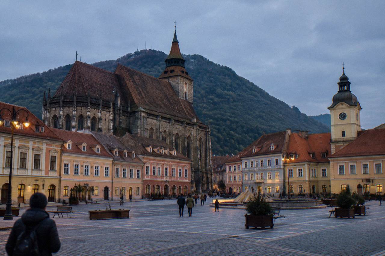 A colourful old town square in Brașov surrounded by red-roofed merchant houses under an overcast sky