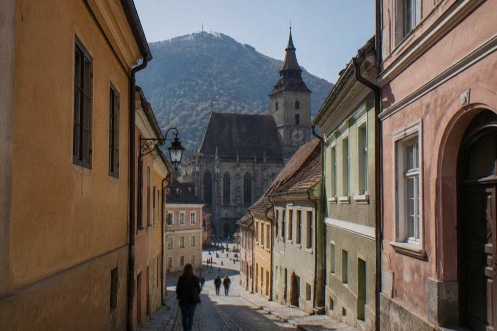 A narrow medieval street in Brașov with tall coloured houses and the shadow of the surrounding hills