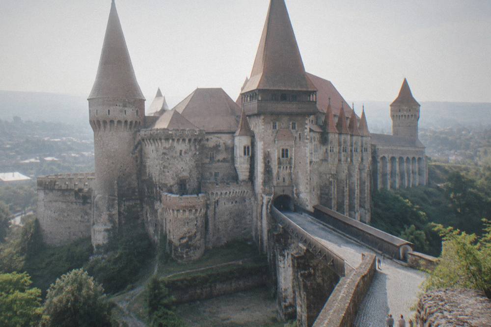 Stone bridge leading to a fortified castle entrance with tall pointed towers