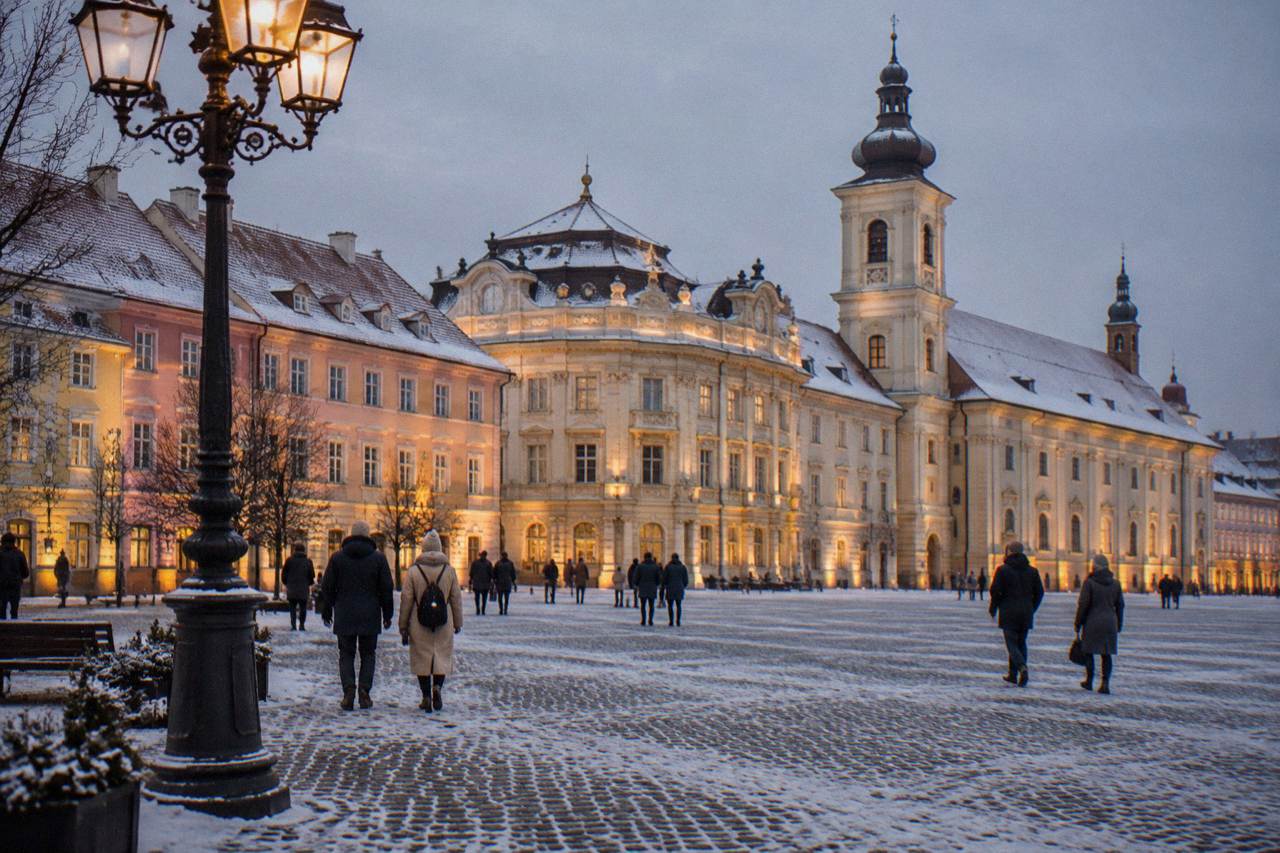 Sibiu's Piața Mare at dusk in winter, with lit facades and a dusting of snow