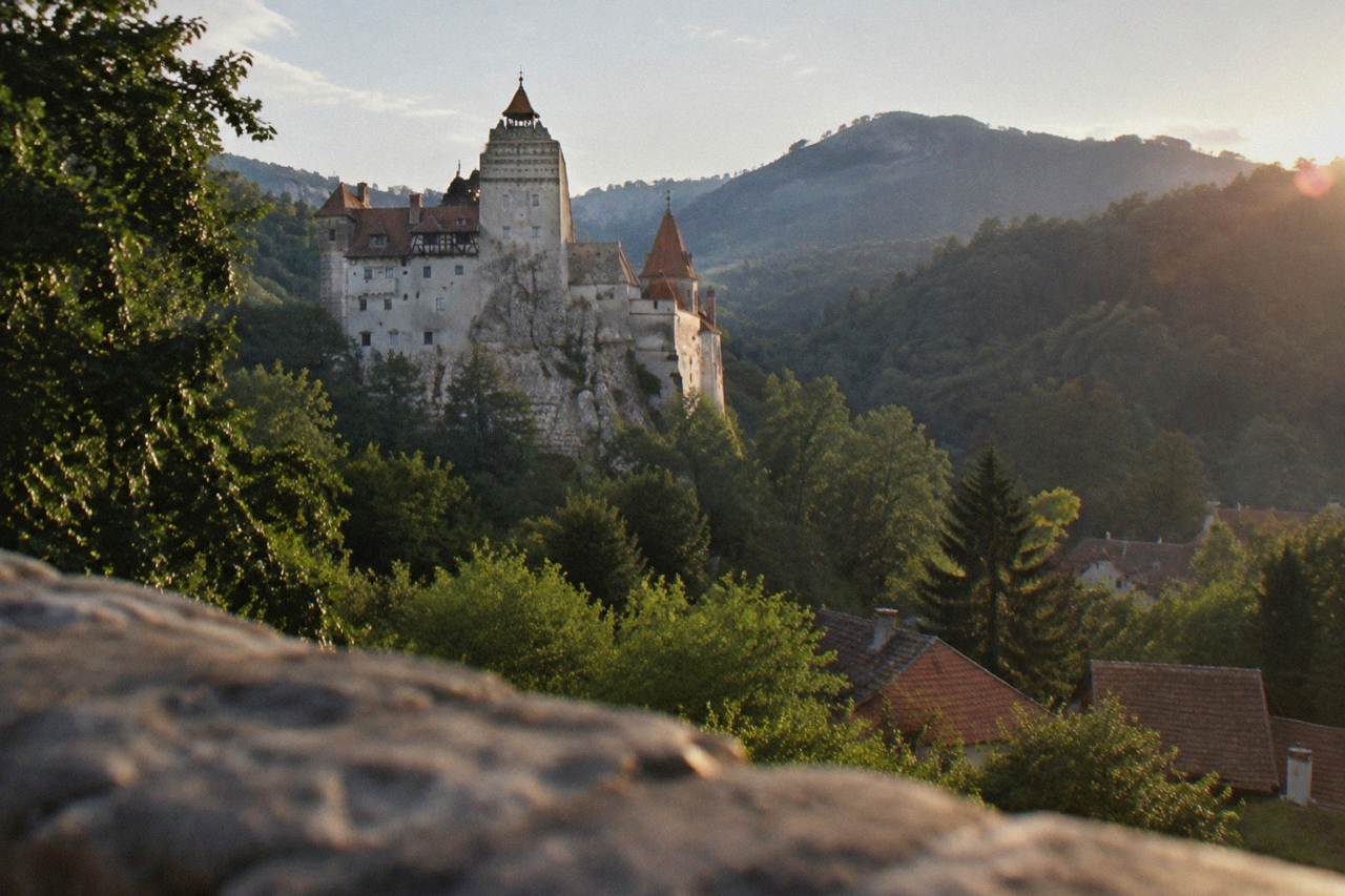 Bran Castle rising above the trees at the edge of a Transylvanian village, with its white towers and red-tiled roofs against the hills