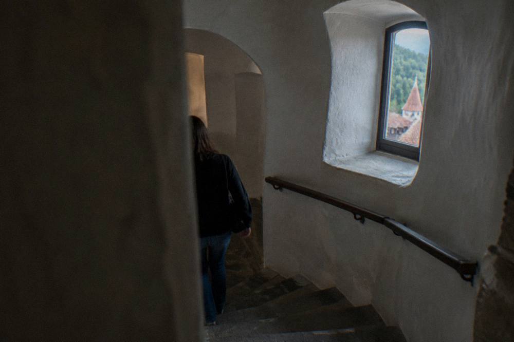 A narrow stone staircase inside a medieval castle, with thick white walls and a small arched window letting in daylight