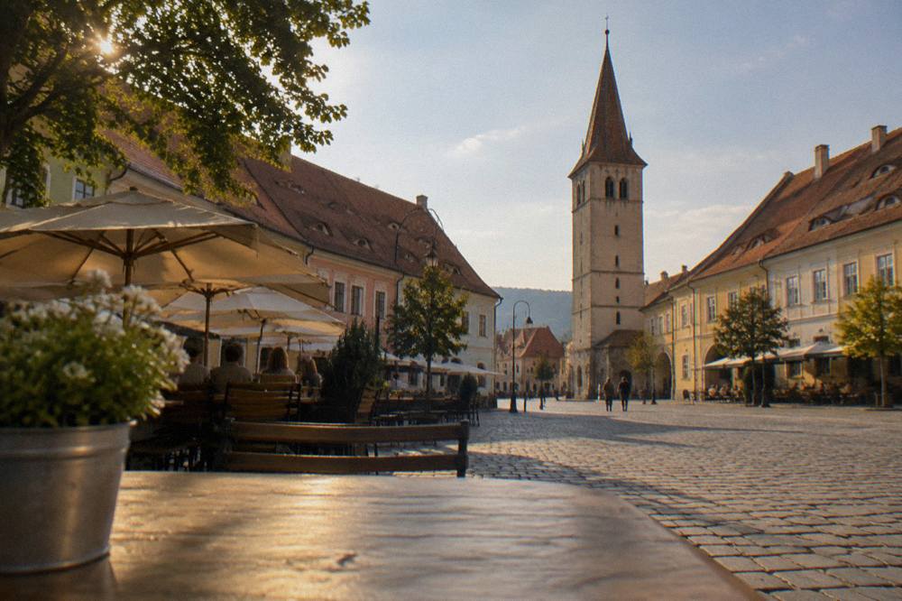 A medieval square in Sibiu with a clock tower and open-air cafe seating in evening light