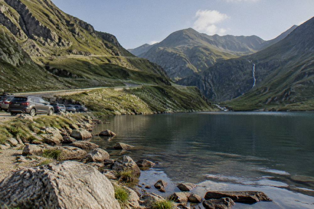 Parked cars and a rocky shoreline along a glacial lake surrounded by steep mountain walls