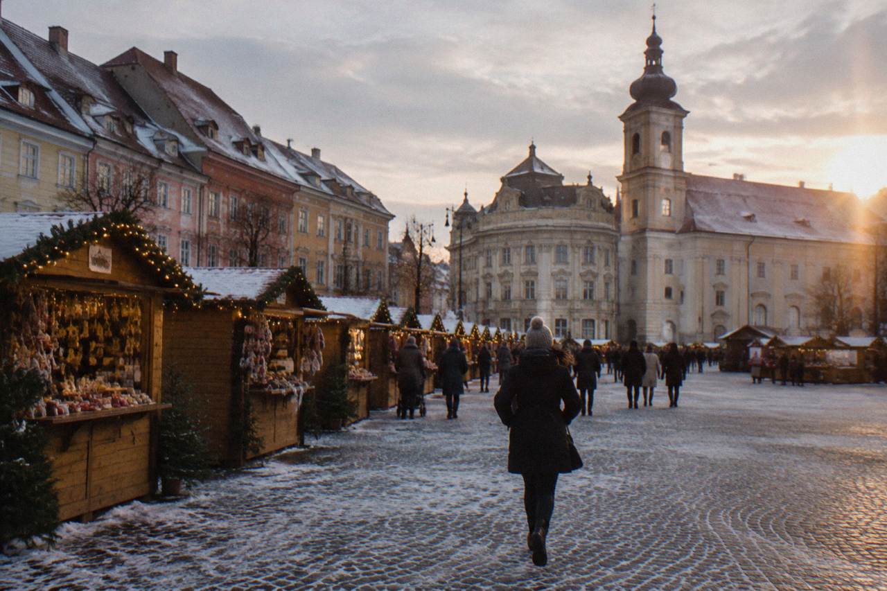 Wooden Christmas market stalls with festive lights lining a large square in Sibiu at dusk