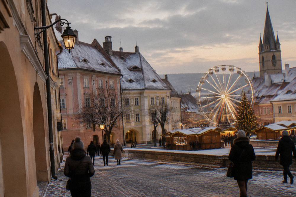 An illuminated Ferris wheel and Christmas lights above rooftops in a Transylvanian old town