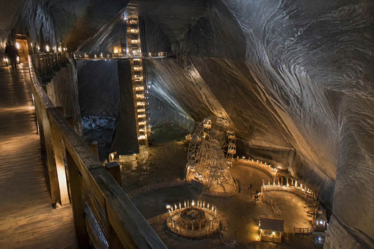 The vast underground chamber of the Turda salt mine lit in warm colours, with a ferris wheel far below on the mine floor