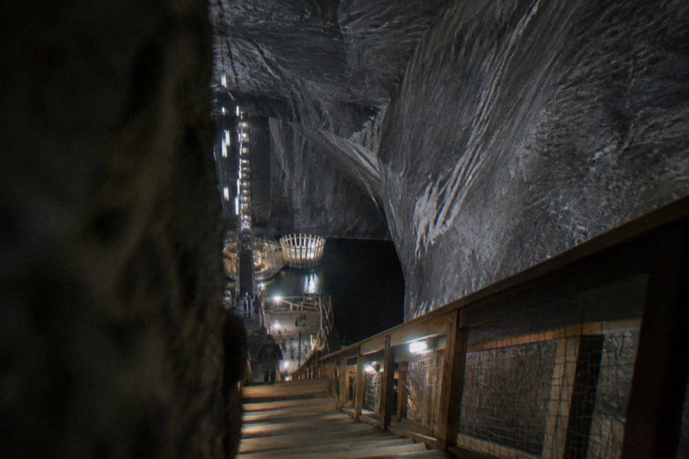 A wooden staircase and walkway descending through a dim rock-cut tunnel inside a historic salt mine