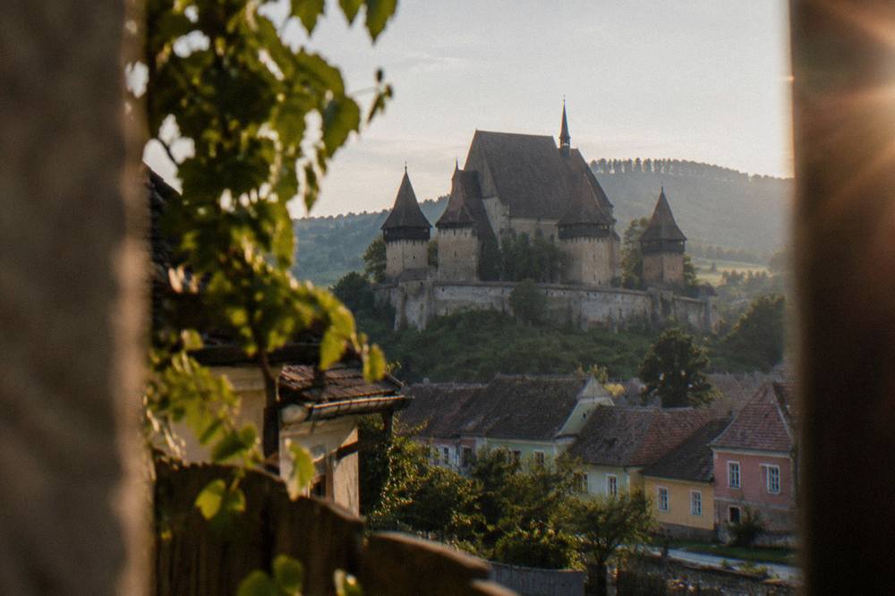 A fortified church with thick defensive walls and towers standing above a Transylvanian village