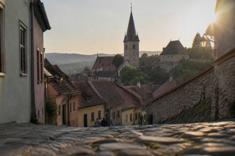 A medieval clock tower rising above red-tiled rooftops in a Transylvanian town