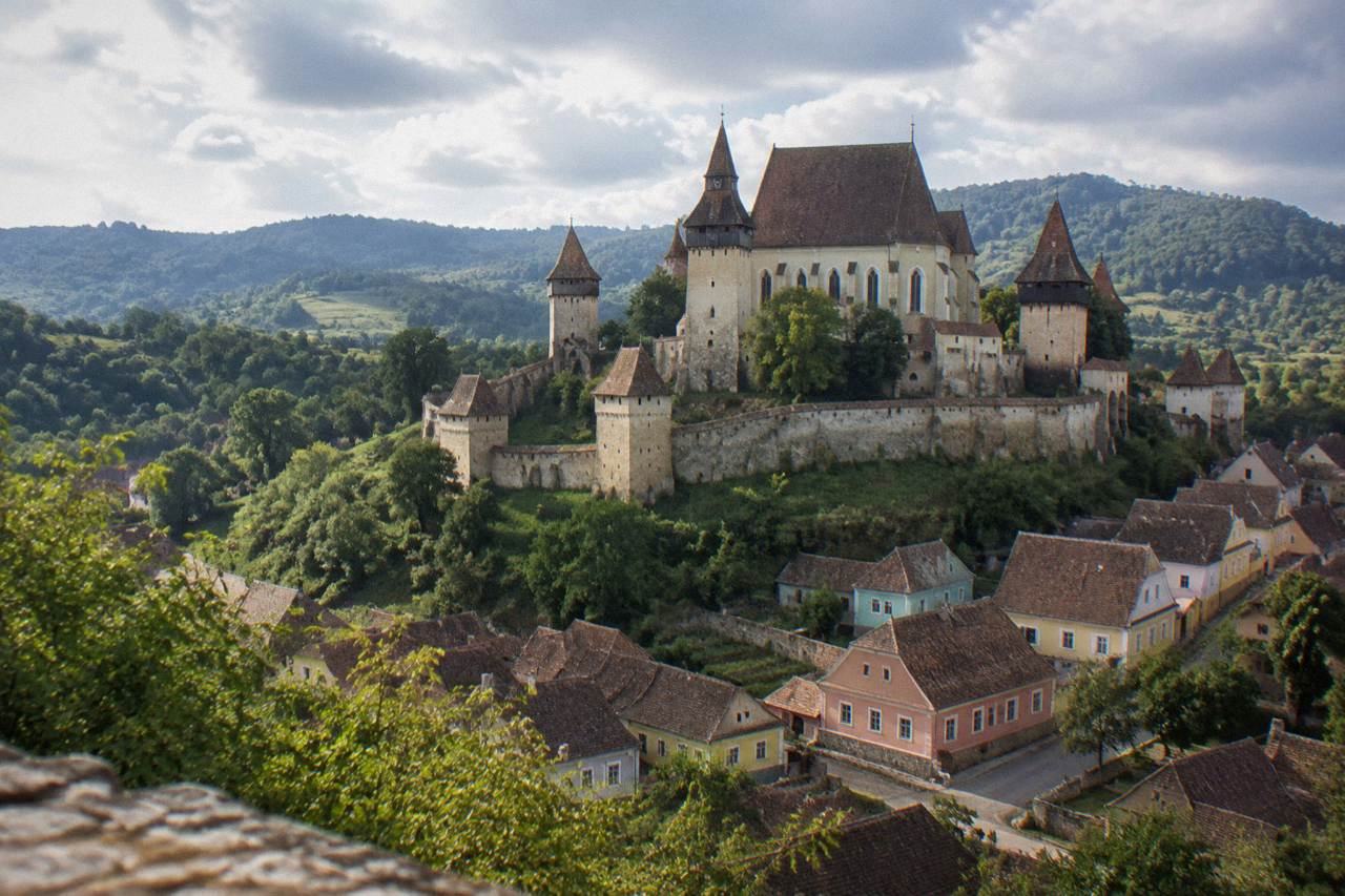 A fortified church with high defensive walls and towers rising above a Transylvanian village