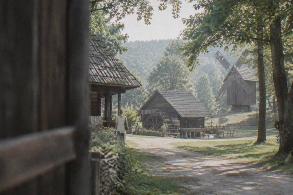 Wooden farmhouses and barns of an open-air village museum beside a dirt lane among trees