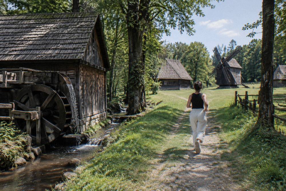 A wooden watermill beside a small stream among trees in an open-air museum