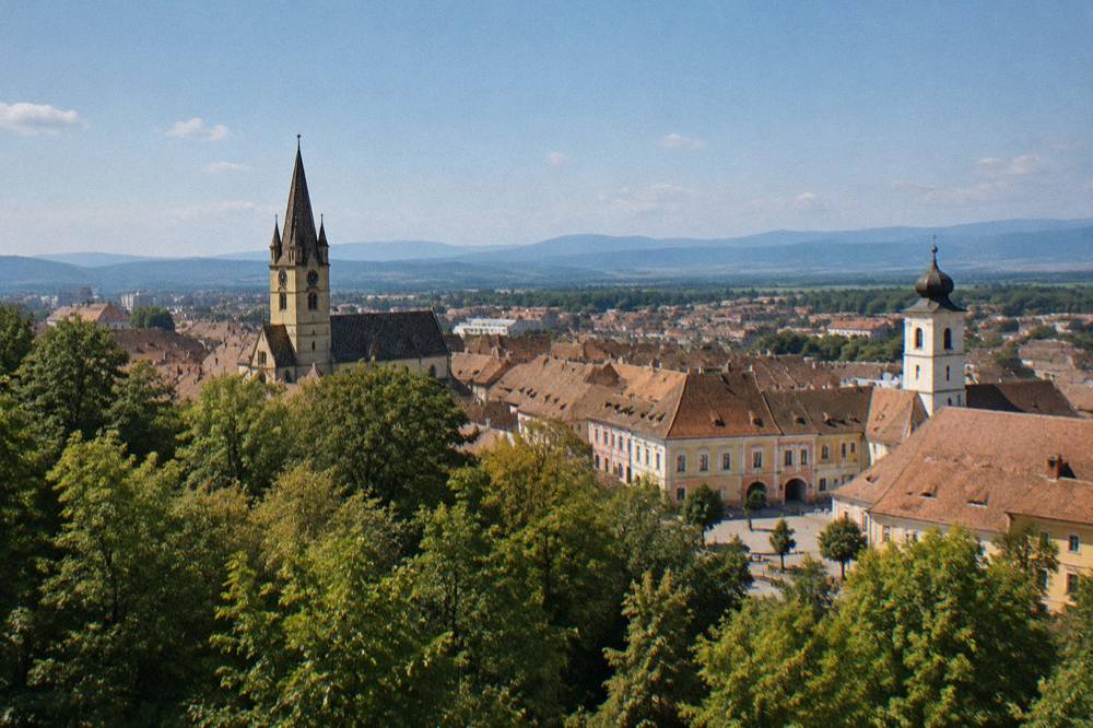 A view over a forest canopy on the edge of Sibiu toward distant blue hills