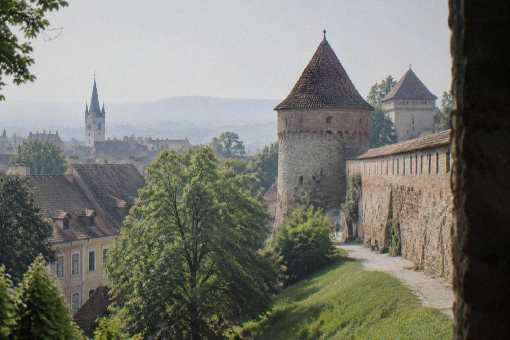 A section of medieval city wall with a round tower above trees and rooftops in Sibiu's Lower Town