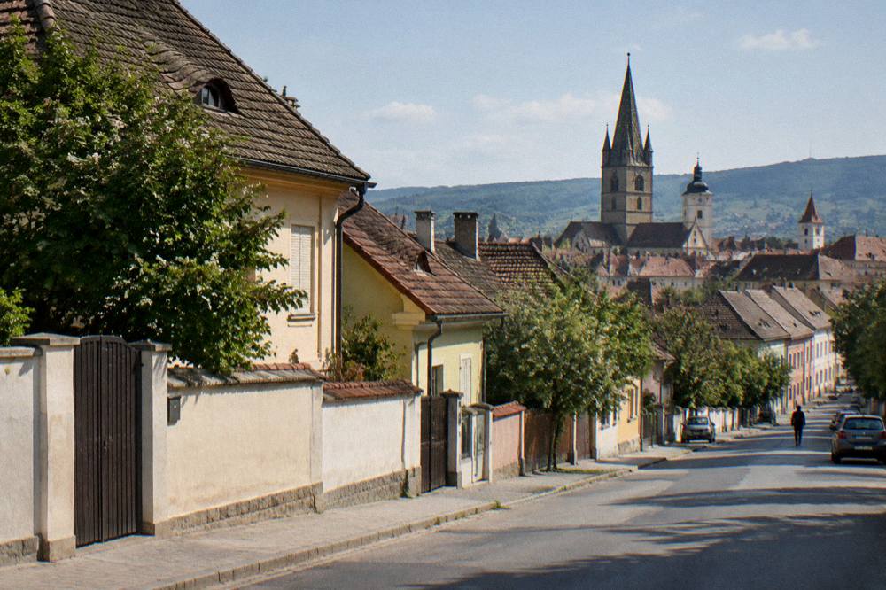 Morning light on a Turnișor street with the towers of Sibiu old town rising above the rooftops