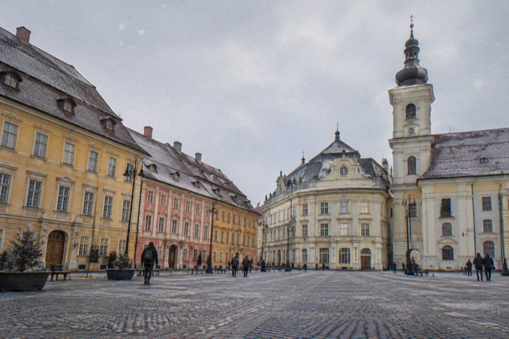 Pastel-coloured townhouses with attic roof windows lining a large square in Sibiu
