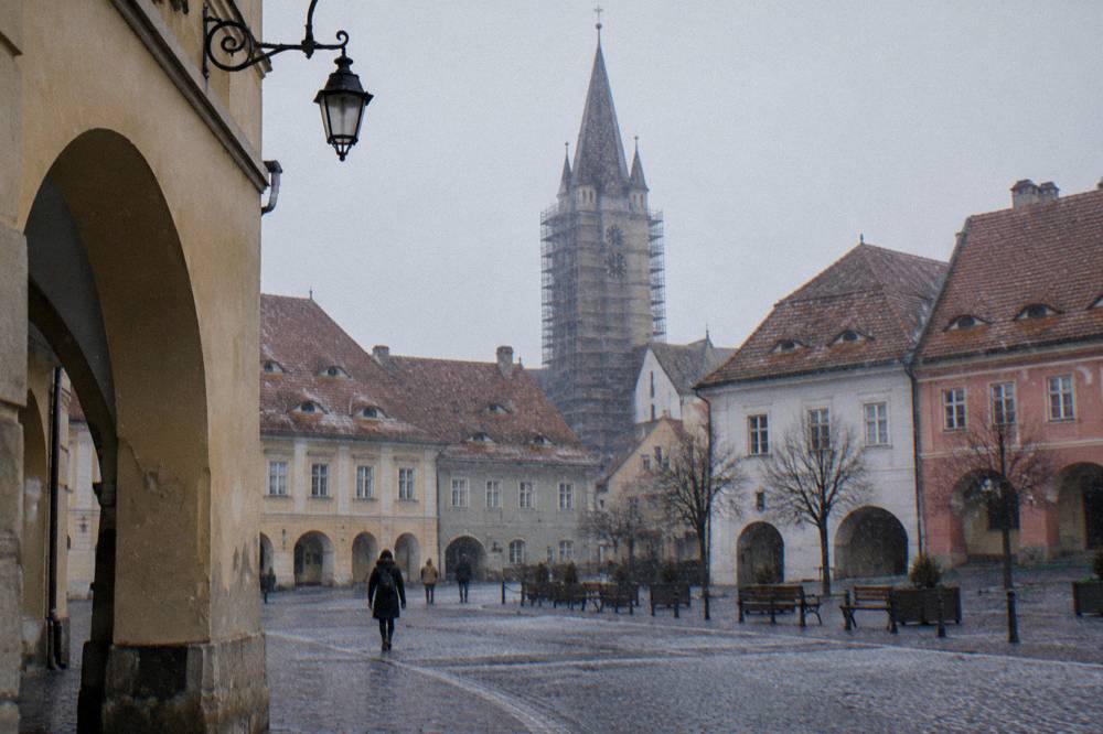 A stone church tower with scaffolding rising between old squares in Sibiu
