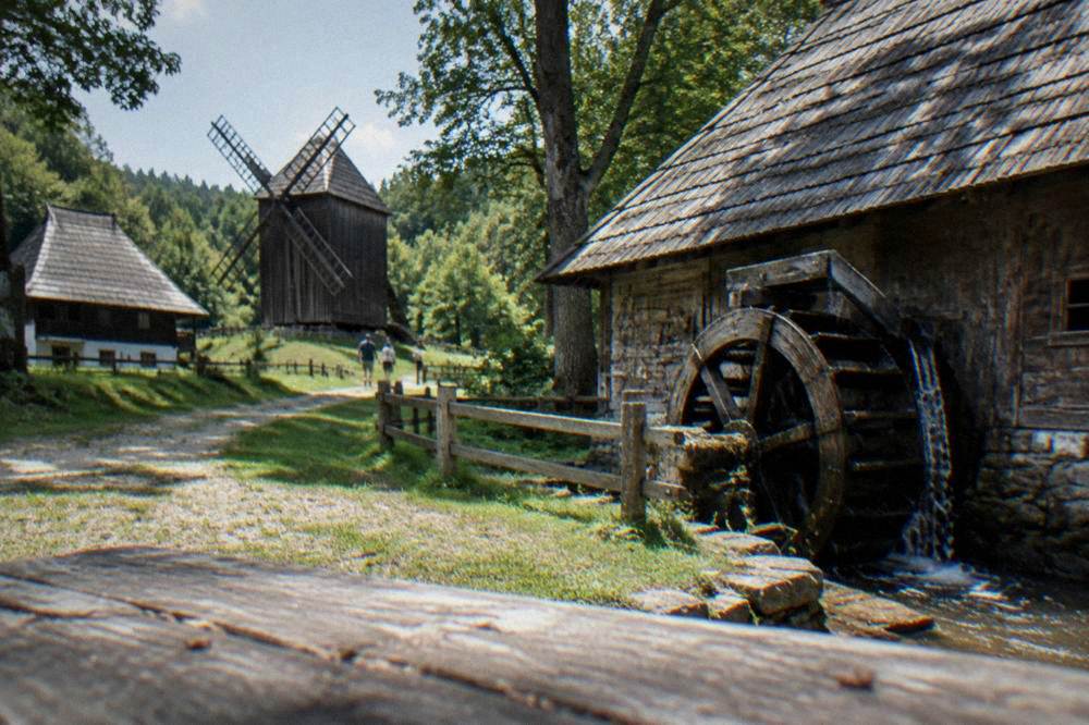 Wooden farmhouses and a windmill stand in an open meadow under a wide sky.