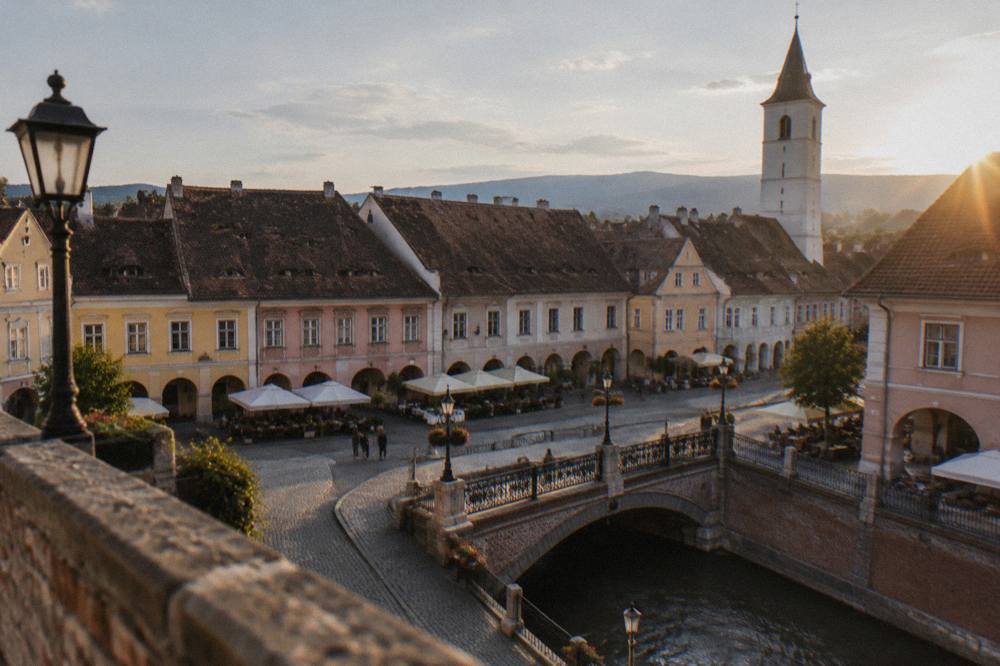 Café tables and historic guild houses along Piața Mică beneath the bridge