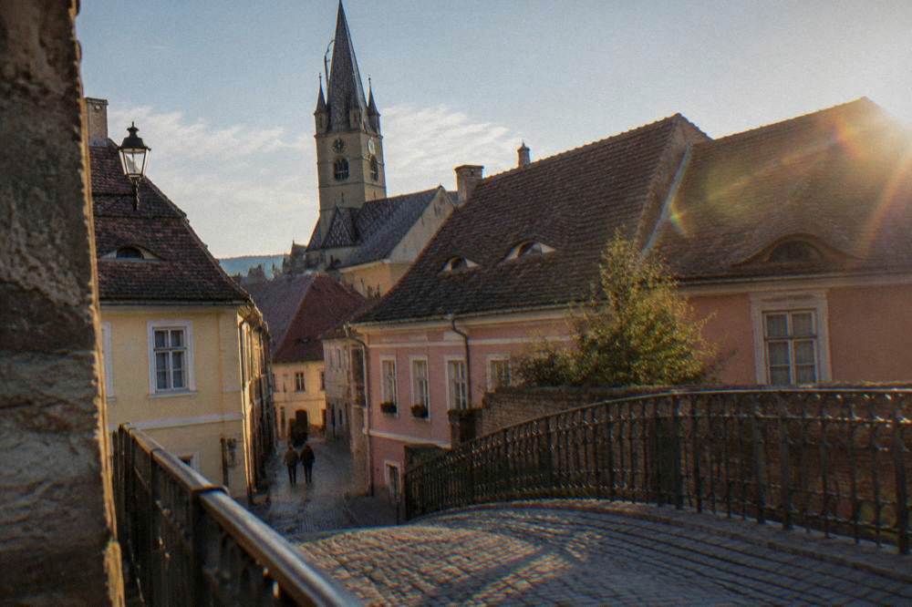 A low cast-iron bridge crosses a stone passage between two old buildings at dusk.