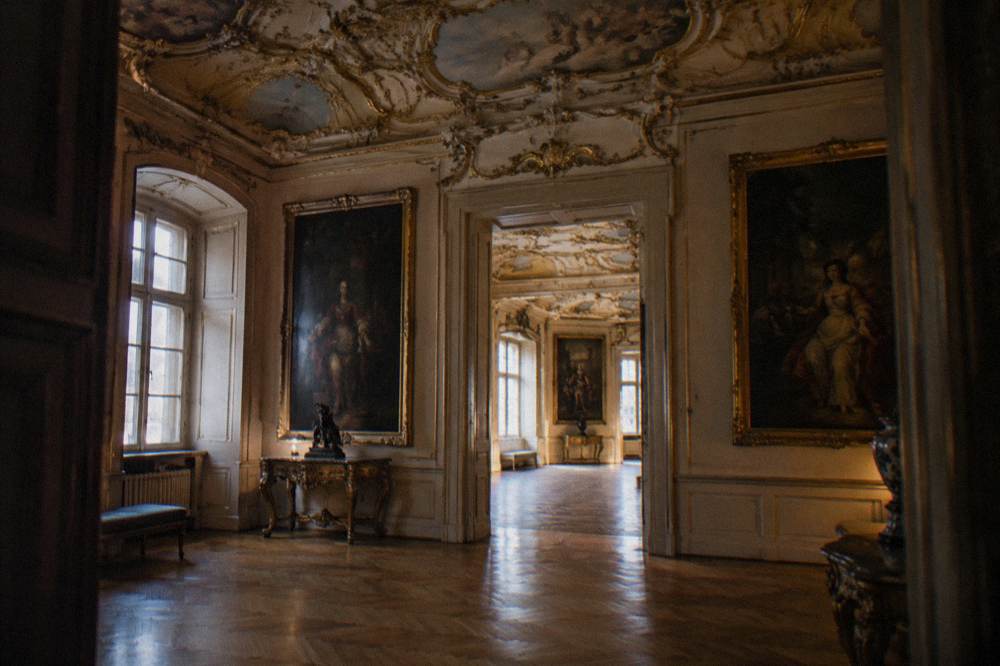 Ornate baroque interior room with gilded stucco ceiling and framed paintings