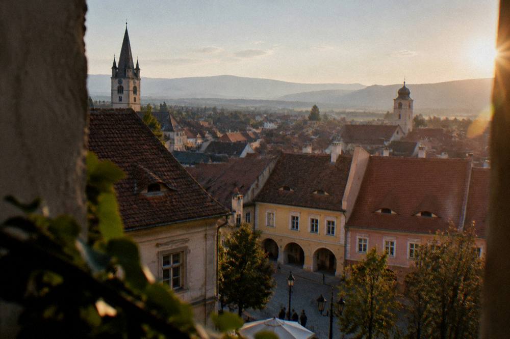 Wide view over red rooftops of a Transylvanian old town toward distant hills