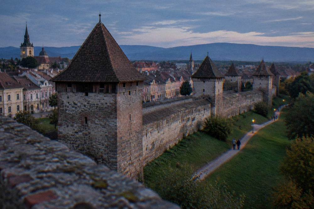 An old stone defensive wall stands with a round tower beside it.