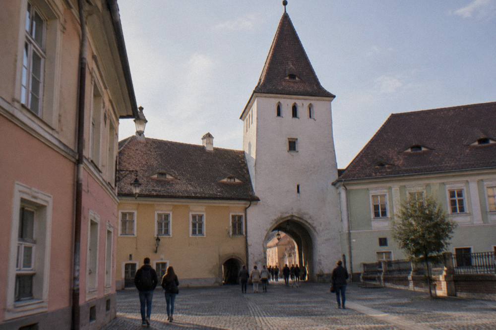 Tourists walking through the arched passage at the base of the Council Tower between two cobbled squares