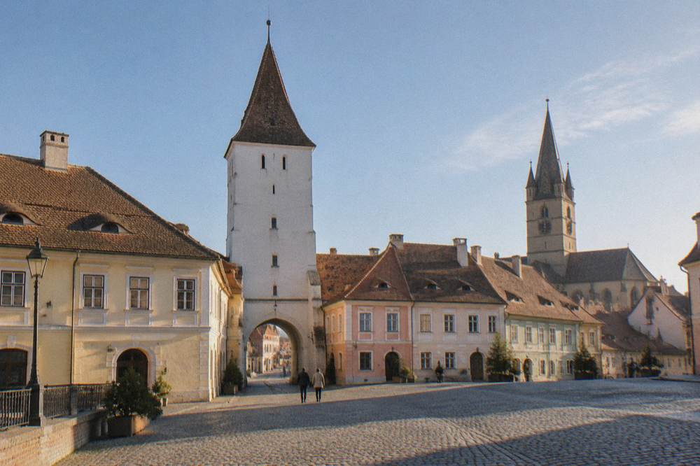 A Gothic church tower seen from a cobbled square with old houses and a church spire in the background