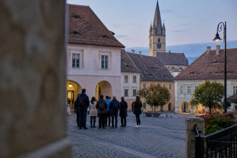 A guided group of visitors standing in a cobbled square of a Transylvanian old town