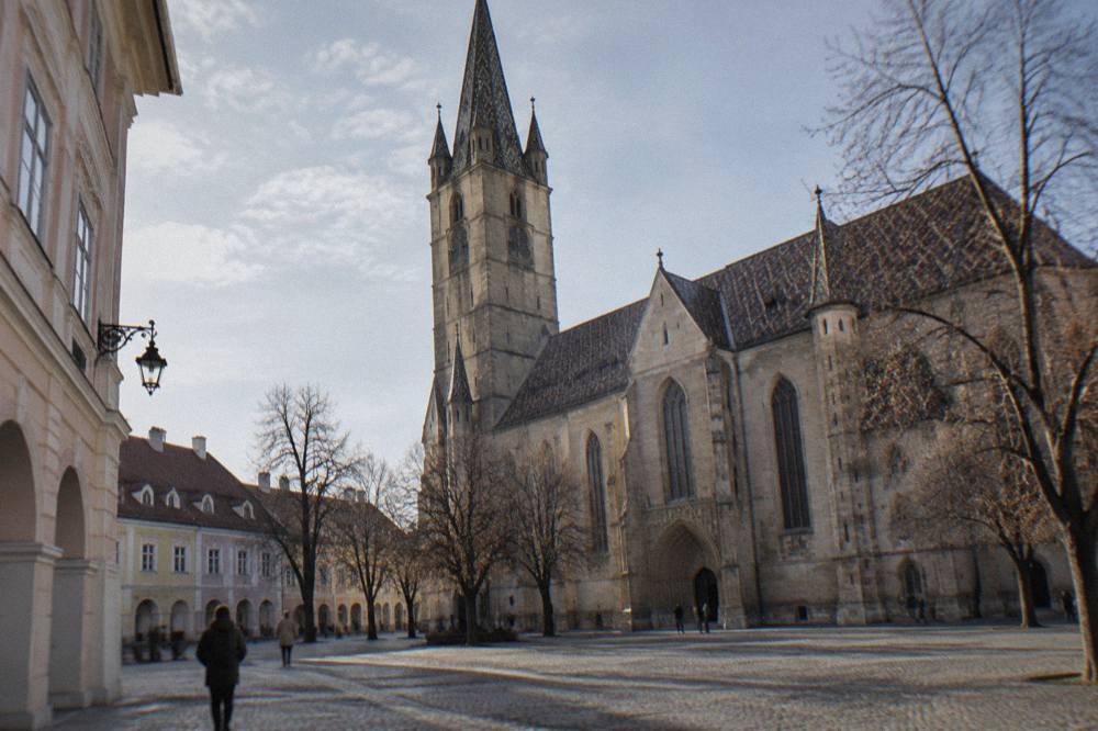 Stone gothic portal and buttresses of a historic church seen from a cobbled square