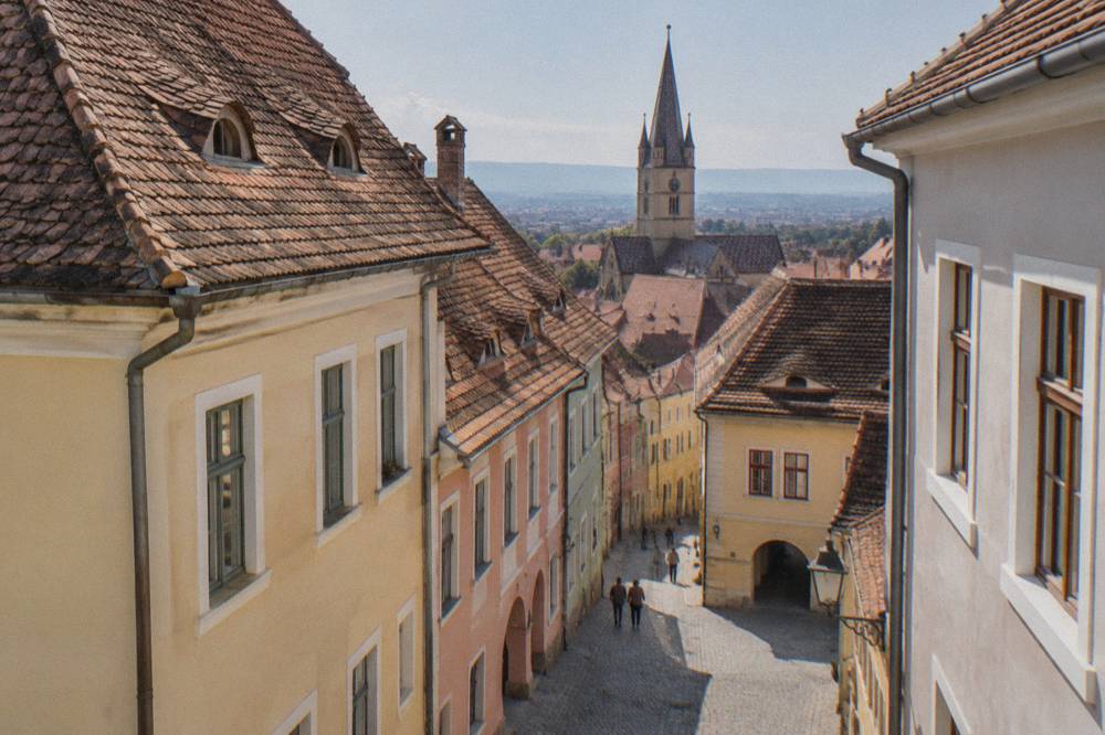 Pastel coloured historic houses and a church steeple seen down a narrow old town street