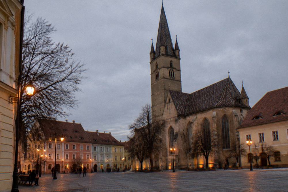 Historic square at dusk with warm street lights and a gothic tower silhouette