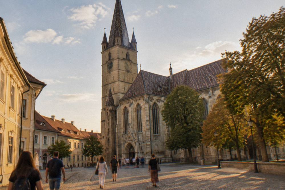 Tourists walking across a cobbled square toward a gothic church entrance in warm afternoon light