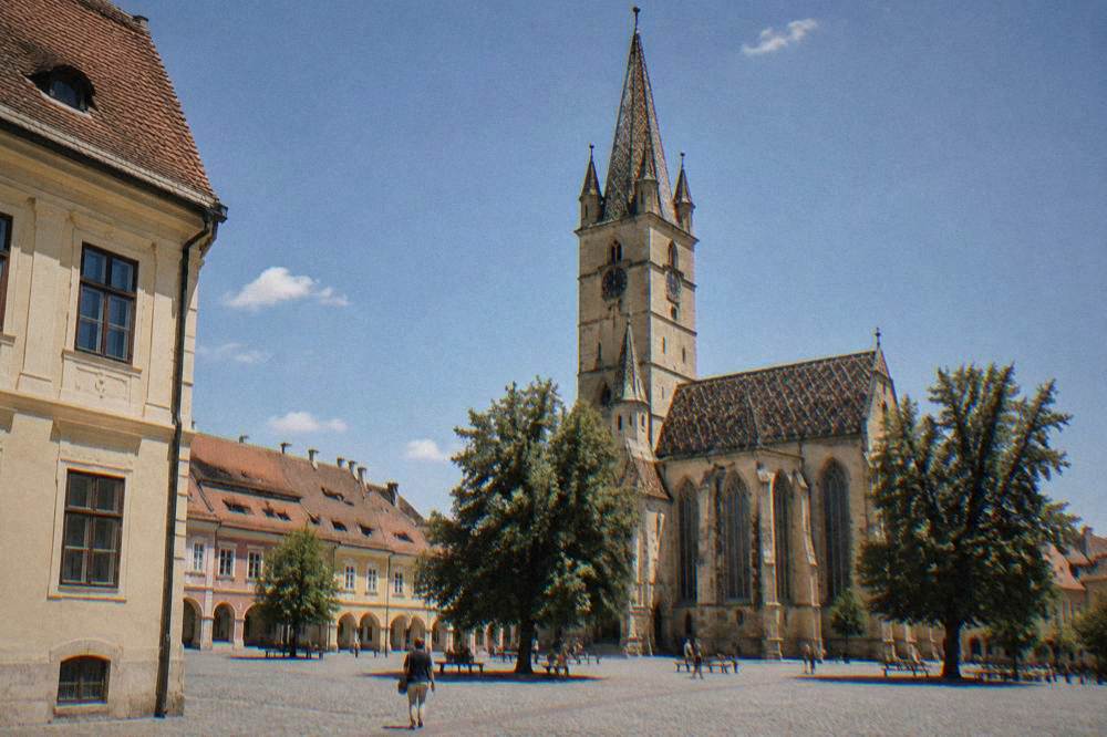 A tall Gothic church tower rising over a quiet cobbled square under a clear sky.