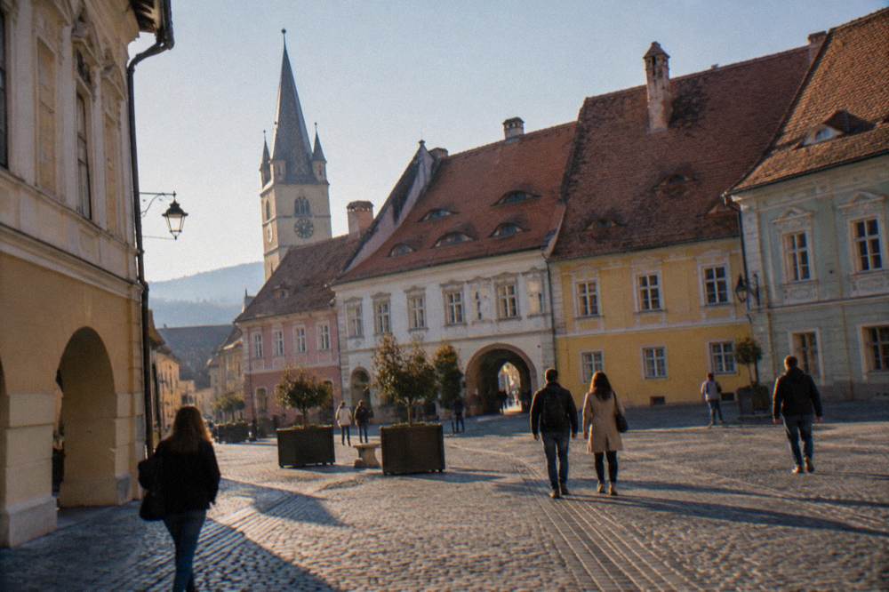 Visitors walking between museum buildings on a cobbled Sibiu square on a bright day