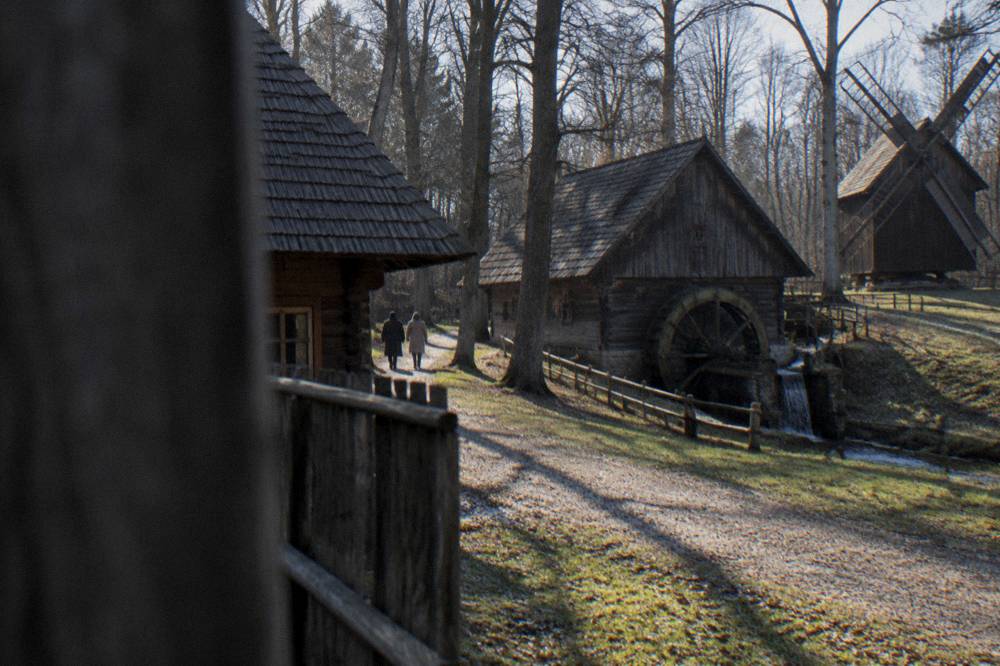 Wooden village houses and a watermill along a lane in an open-air museum in a forest park