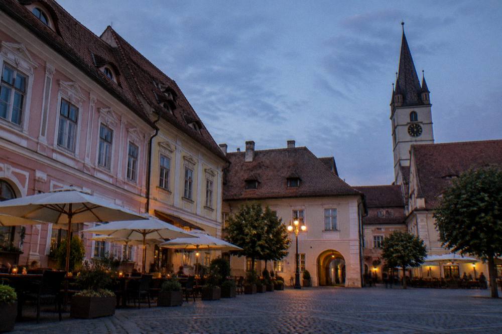A quiet Sibiu square in evening light with cafe tables and historic facades