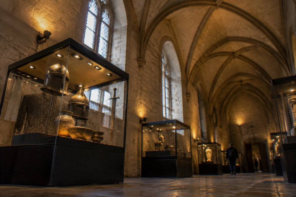 A vaulted stone interior hall with display cases of medieval artefacts