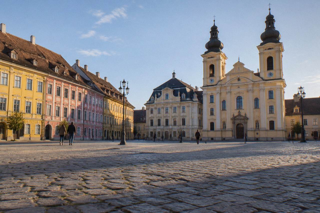 Baroque church facade with twin towers standing along the edge of a large square in Sibiu
