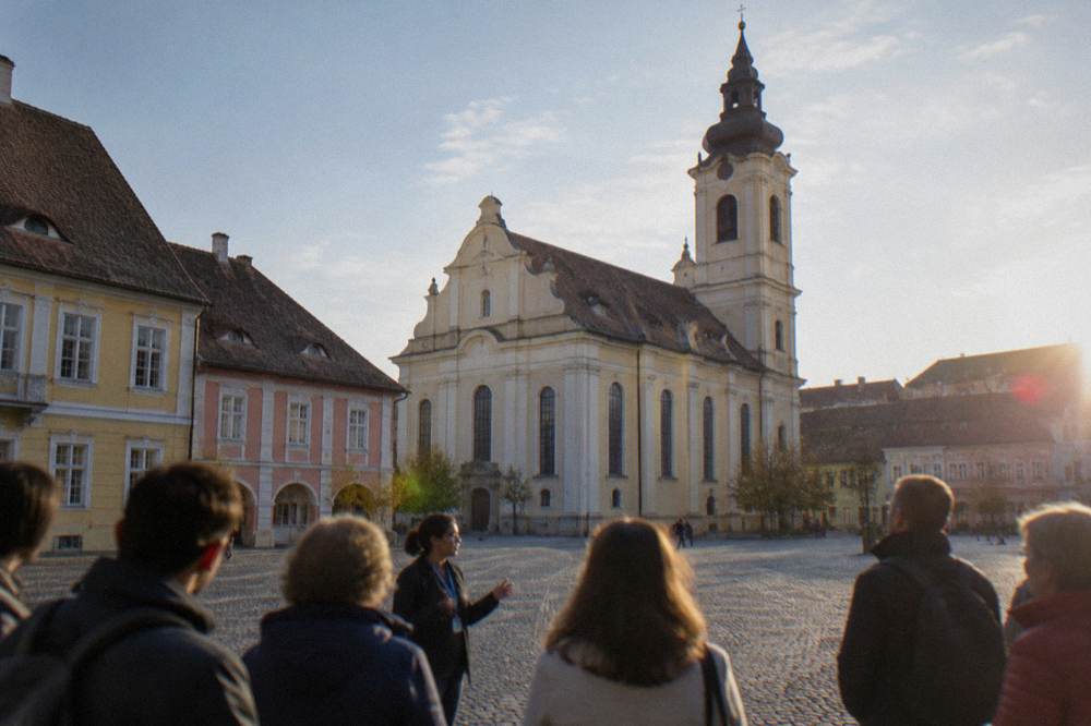 A guided group of visitors standing in a historic square listening to a guide